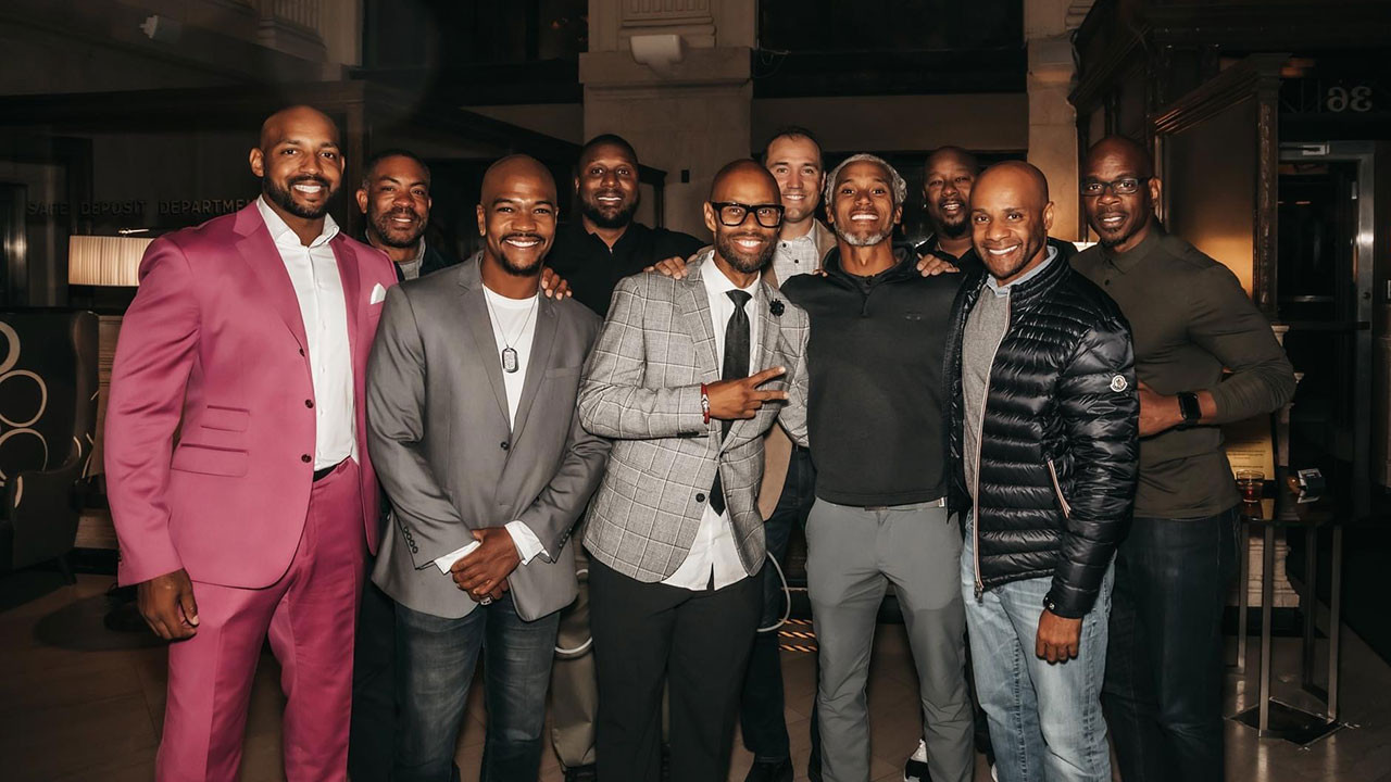 Group of smiling men in semi-formal and casual attire posing at a Brave Men Inc. event celebration.